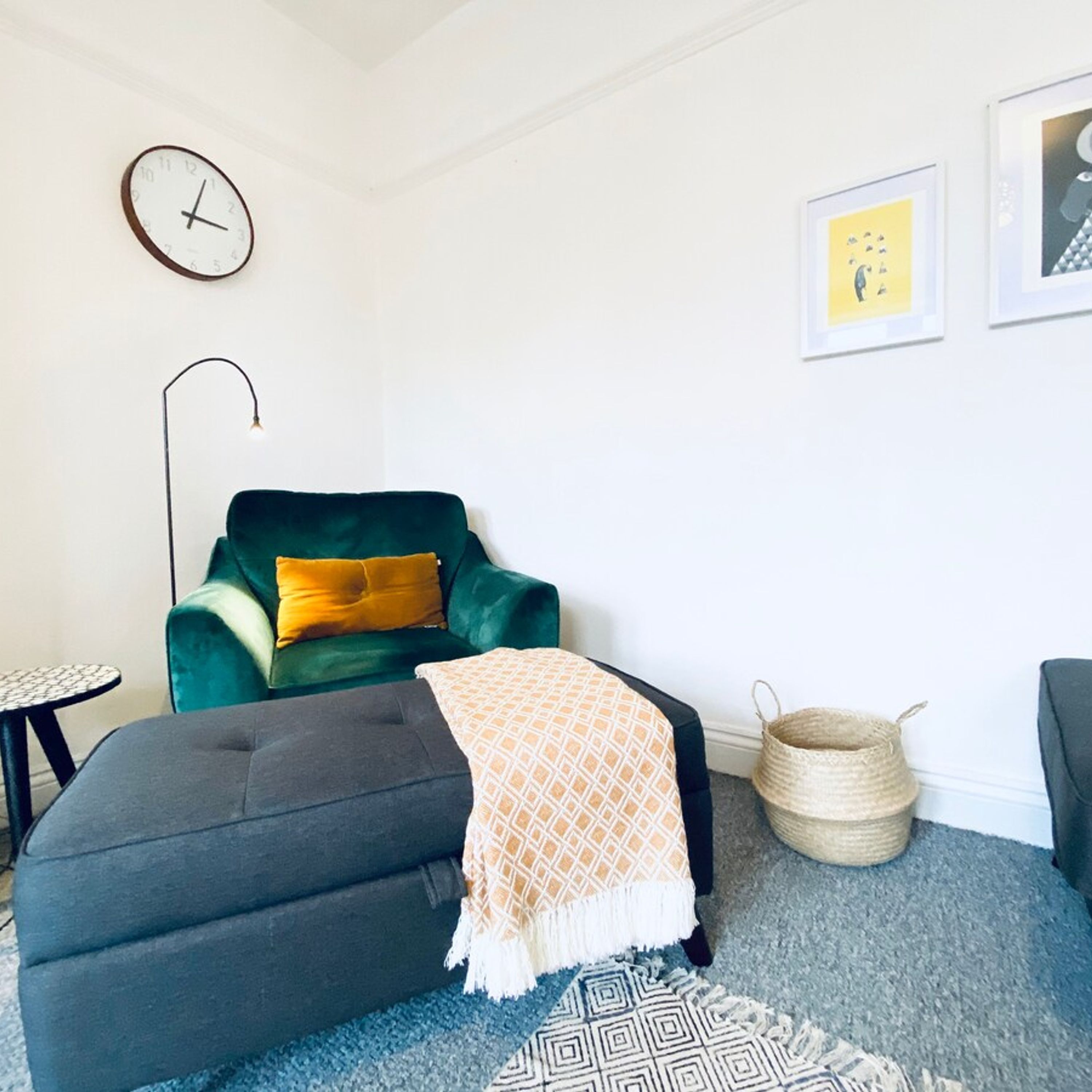 Ein modernes Wohnzimmer mit einem grünen Sessel, einem grauen Sofa, einem kleinen runden Tisch, einer Stehlampe und einem gewebten Korb.