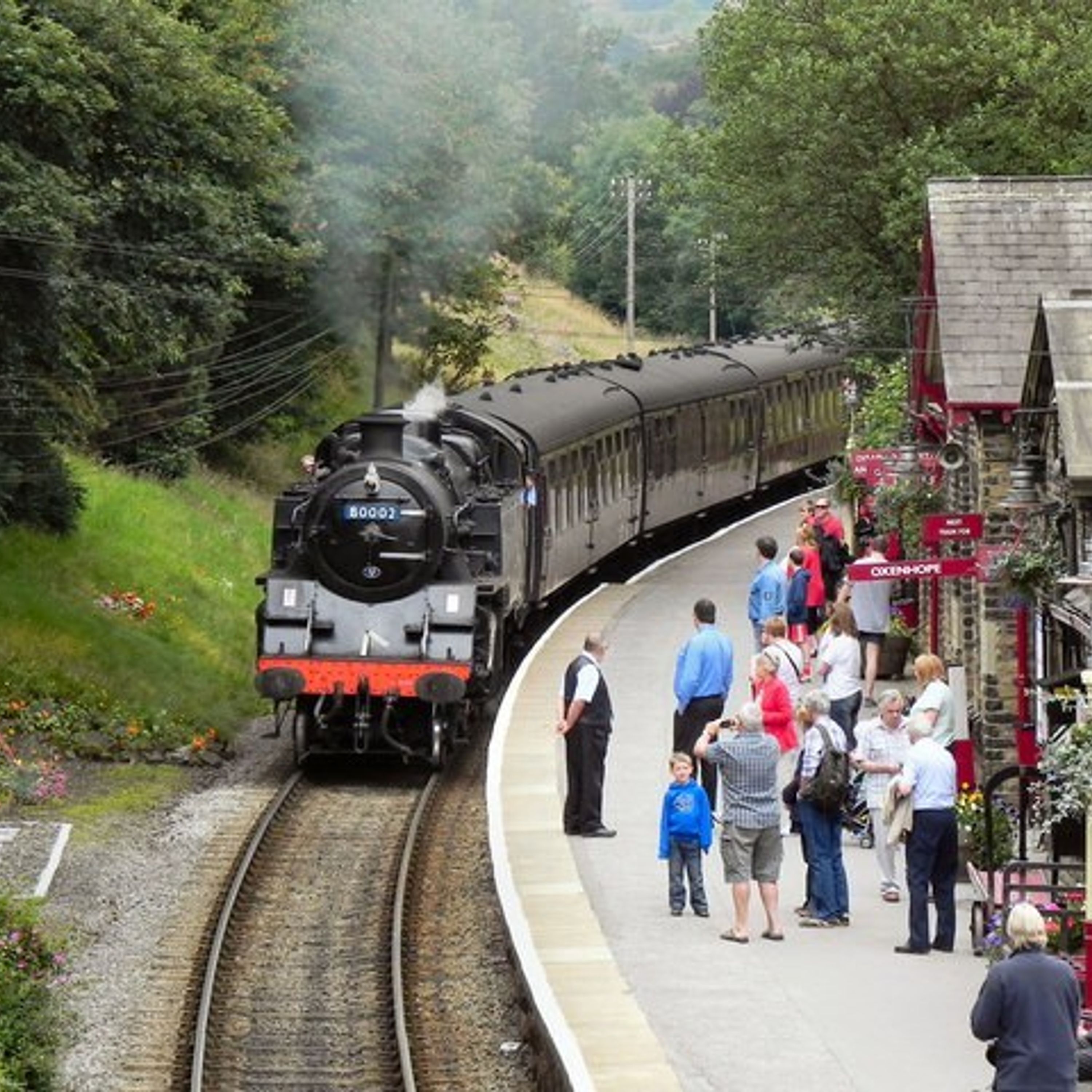A steam train at a station with passengers waiting on the platform.