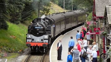 A steam train at a station with passengers waiting on the platform.