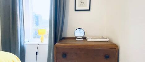 Une chambre avec une commode en bois, un miroir rond et un tableau encadré accroché au mur.