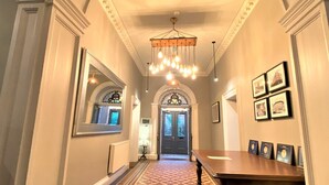A hallway with a patterned floor, a wooden table with framed awards, and a chandelier. - Claremont The Smeaton (Leeds)