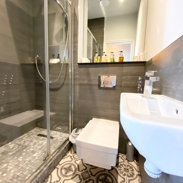 A modern bathroom with a glass shower enclosure, a white sink, and a patterned floor.