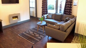 A modern living room with a sofa, a flat-screen TV, a fireplace, and a patterned rug. - Coach House Stables in Leeds (Leeds)