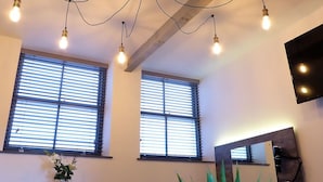 A room with two large windows, a dining table with chairs, a potted plant, and a mounted flat-screen TV. - Coach House Stables in Leeds (Leeds)