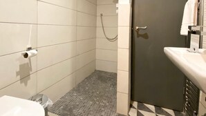 A bathroom with a toilet, a shower area with a tiled floor, and a sink with a towel rack. - Coach House Studio in Leeds (Leeds)