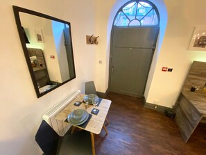 A dining area with a table set for two, a mirror, a radiator, a door, and a view through an arched window. - Coach House Studio in Leeds (Leeds)