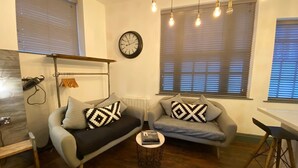 A modern living room with two sofas, a coffee table, a clock, and a window with blinds. - Coach House Studio in Leeds (Leeds)