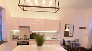 A modern kitchen with white cabinets, a central island with stools, a hanging light fixture, and a small dining area with a table and chairs. - Coach House Studio in Leeds (Leeds)