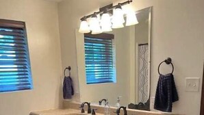 A bathroom with a double sink vanity, a large mirror, and a window with blinds.