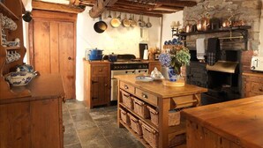 A rustic kitchen with wooden cabinets, a stove, hanging pots, and a stone wall. - Summerhill Cottage Windermere The Lake District (Windermere)