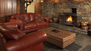 A cozy living room with a stone fireplace, leather sofa, and a woven ottoman. - Summerhill Cottage Windermere The Lake District (Windermere)