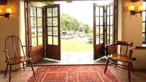 A room with a large open doorway leading to a garden, two wooden chairs, and a red patterned rug. - Summerhill Cottage Windermere The Lake District (Windermere)