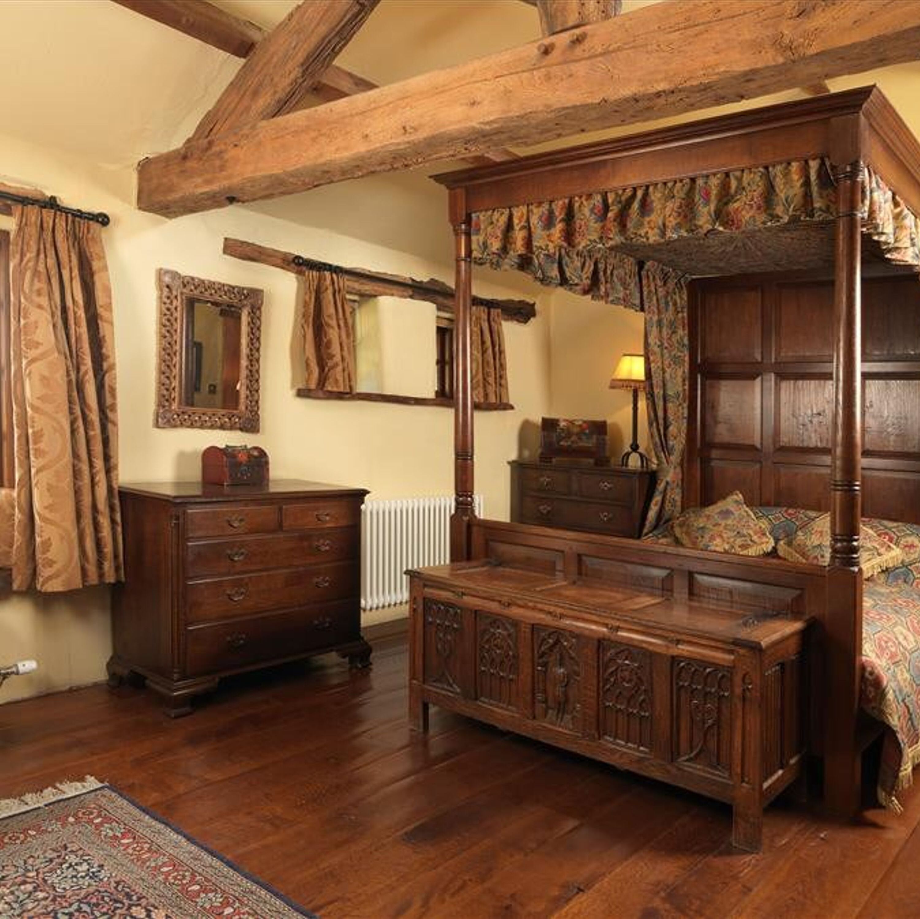 A traditional four-poster bed with a canopy, wooden dresser, and a mirror on the wall.