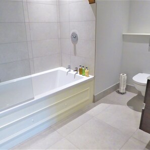 A modern bathroom with a freestanding bathtub, a toilet, and a shelf with toiletries. - Town Hall Lofts Flat 1 Settle (Settle)