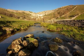 A river flowing through a valley with a stone wall on one side and a grassy landscape on the other. - Town Hall Lofts Flat 1 Settle (Settle)