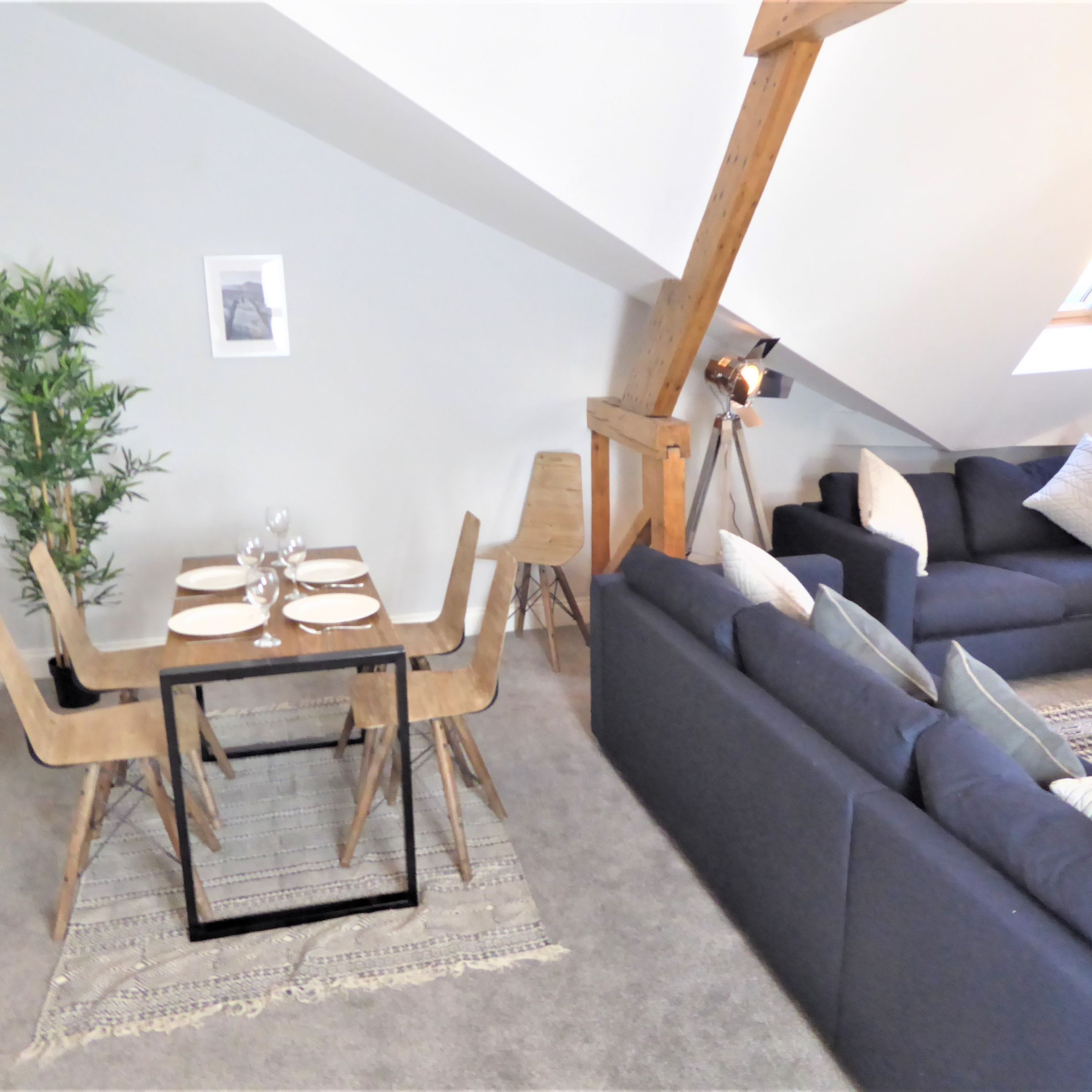 A loft-style living space with a dining area, a sofa, and a tripod-mounted lamp.