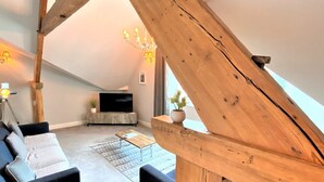 A loft-style living room with exposed wooden beams, a modern sofa set, a flat-screen TV, and a chandelier. - Town Hall Lofts Flat 2 Settle (Settle)