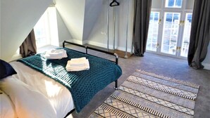A bedroom with a bed, a window with curtains, a hanging rack, and a patterned rug. - Town Hall Lofts Flat 2 Settle (Settle)