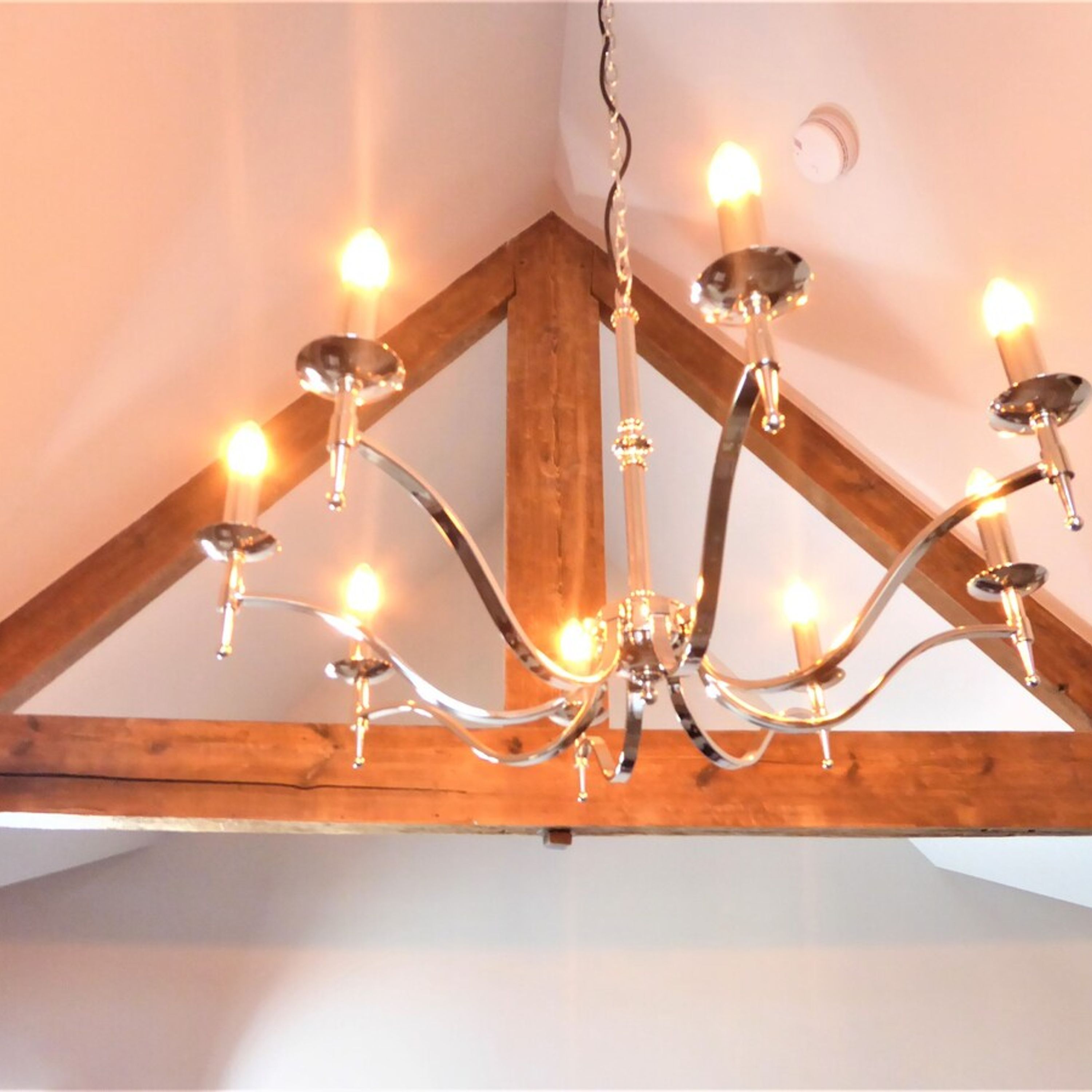 A chandelier with multiple light bulbs hanging from a wooden ceiling structure.