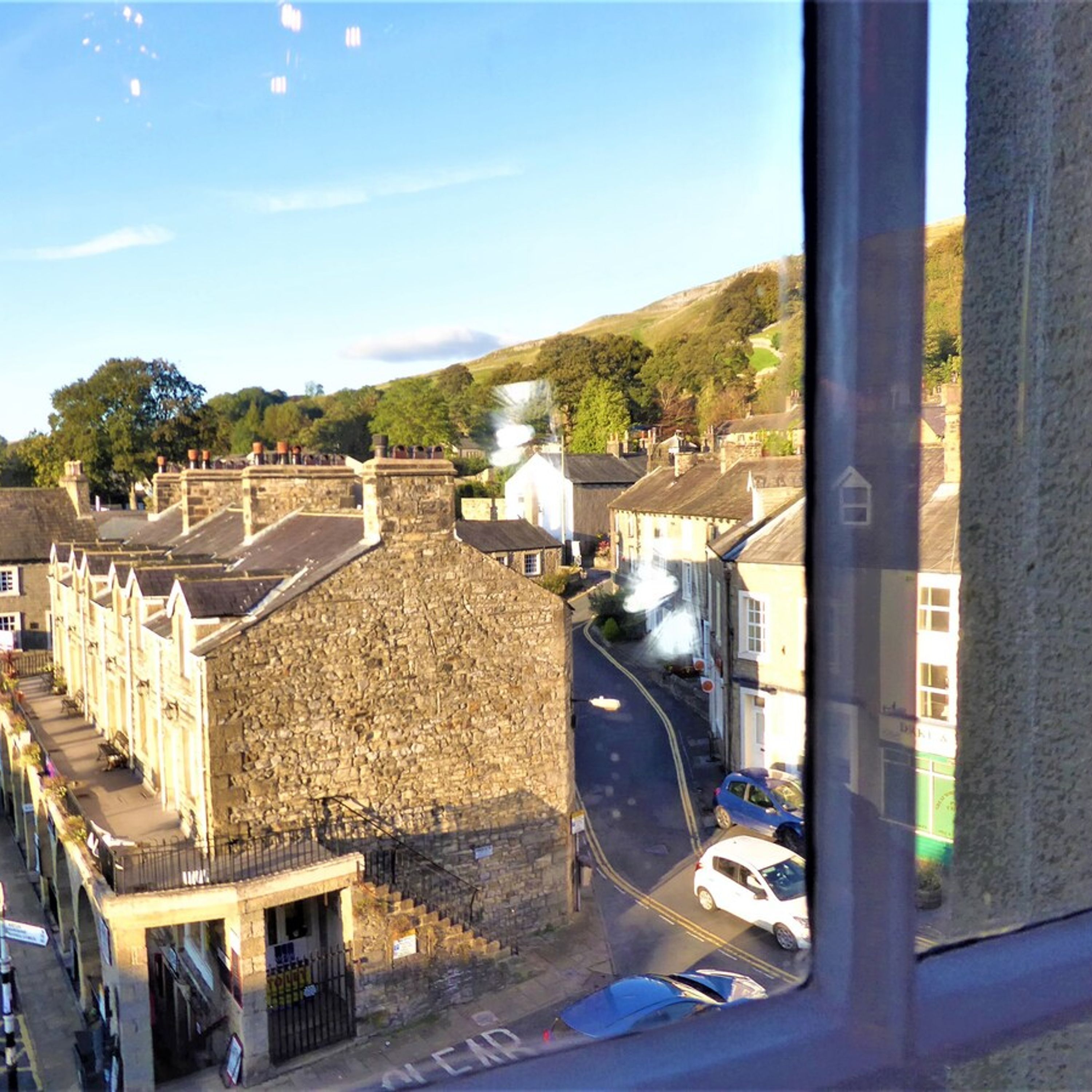 A stone building with a steeply pitched roof, a gated entrance, and a narrow street with parked cars.