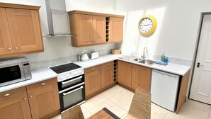 A modern kitchen with wooden cabinets, a built-in oven, a microwave, and a sink. - Town Hall Lofts Flat 2 Settle (Settle)