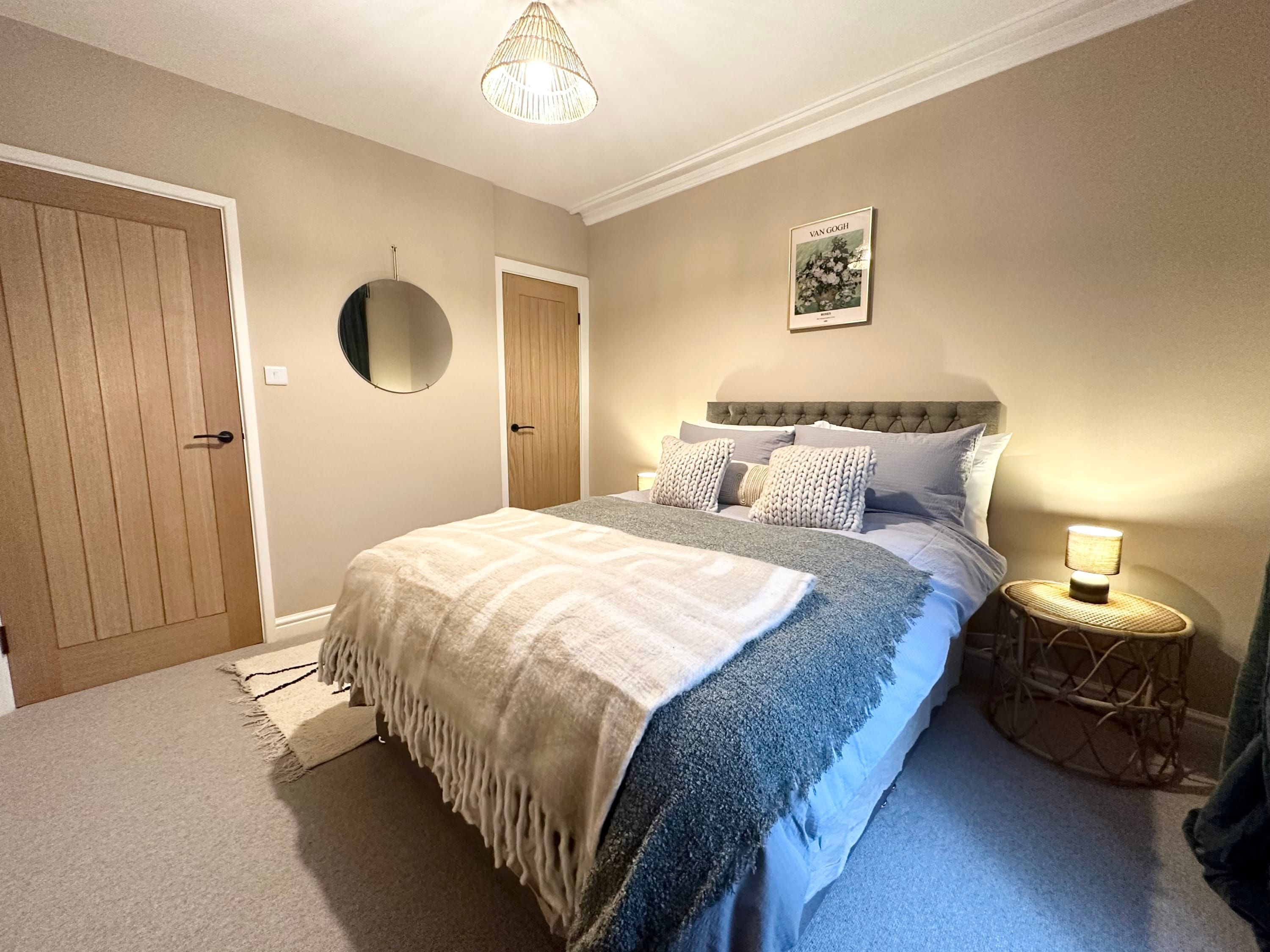 A bedroom with a bed, a bedside lamp, a round mirror, and a framed picture on the wall.