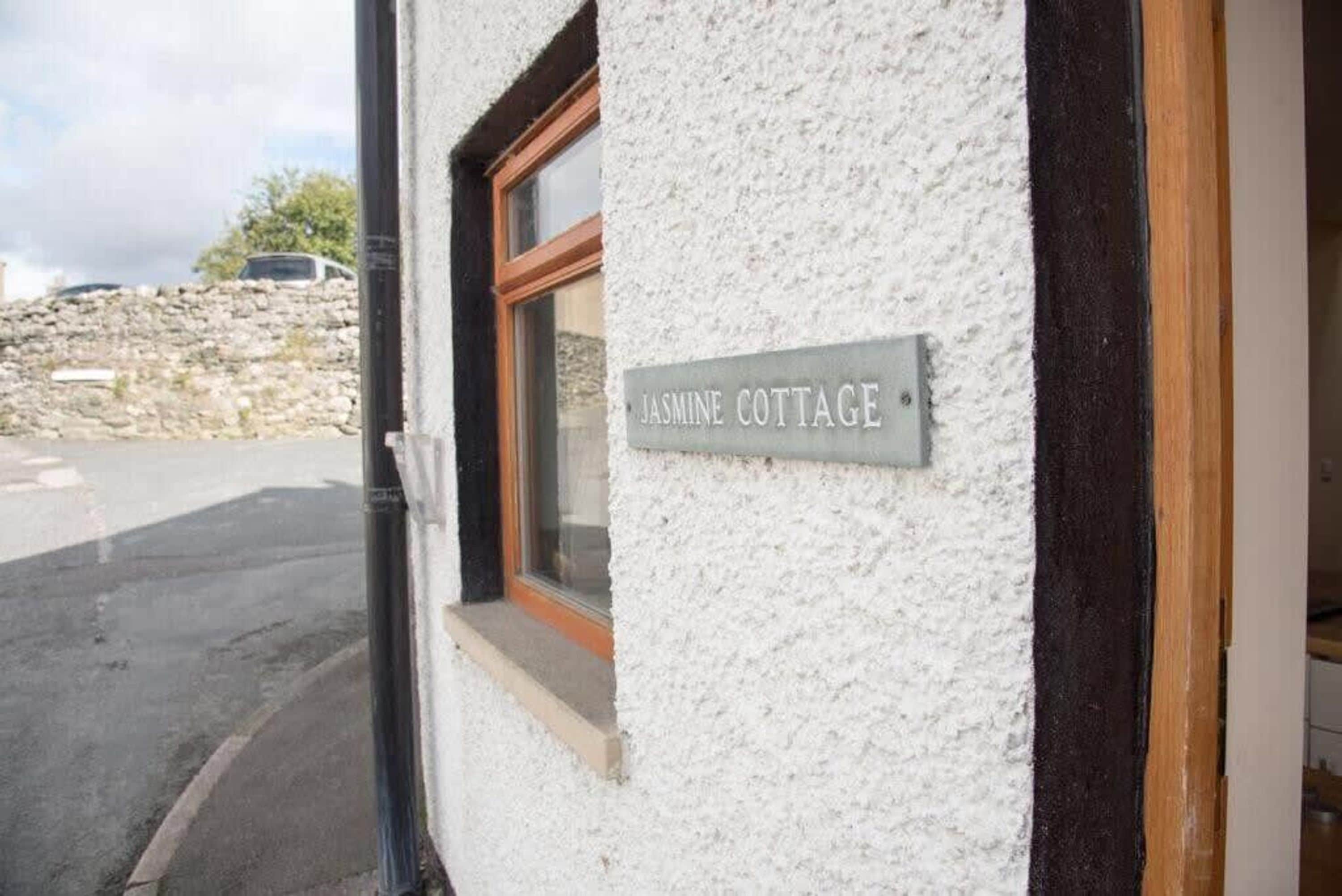 A sign reading "Jasmine Cottage" on a white textured wall.