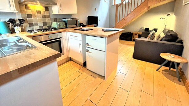 A modern kitchen with a central island, a dining area with a sofa, and a staircase leading to an upper level.