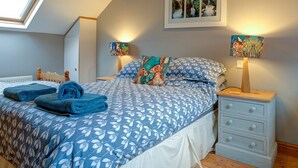 A bedroom with a sloped ceiling, a skylight, a bed with blue floral bedding, two bedside tables with lamps, and a framed picture on the wall.