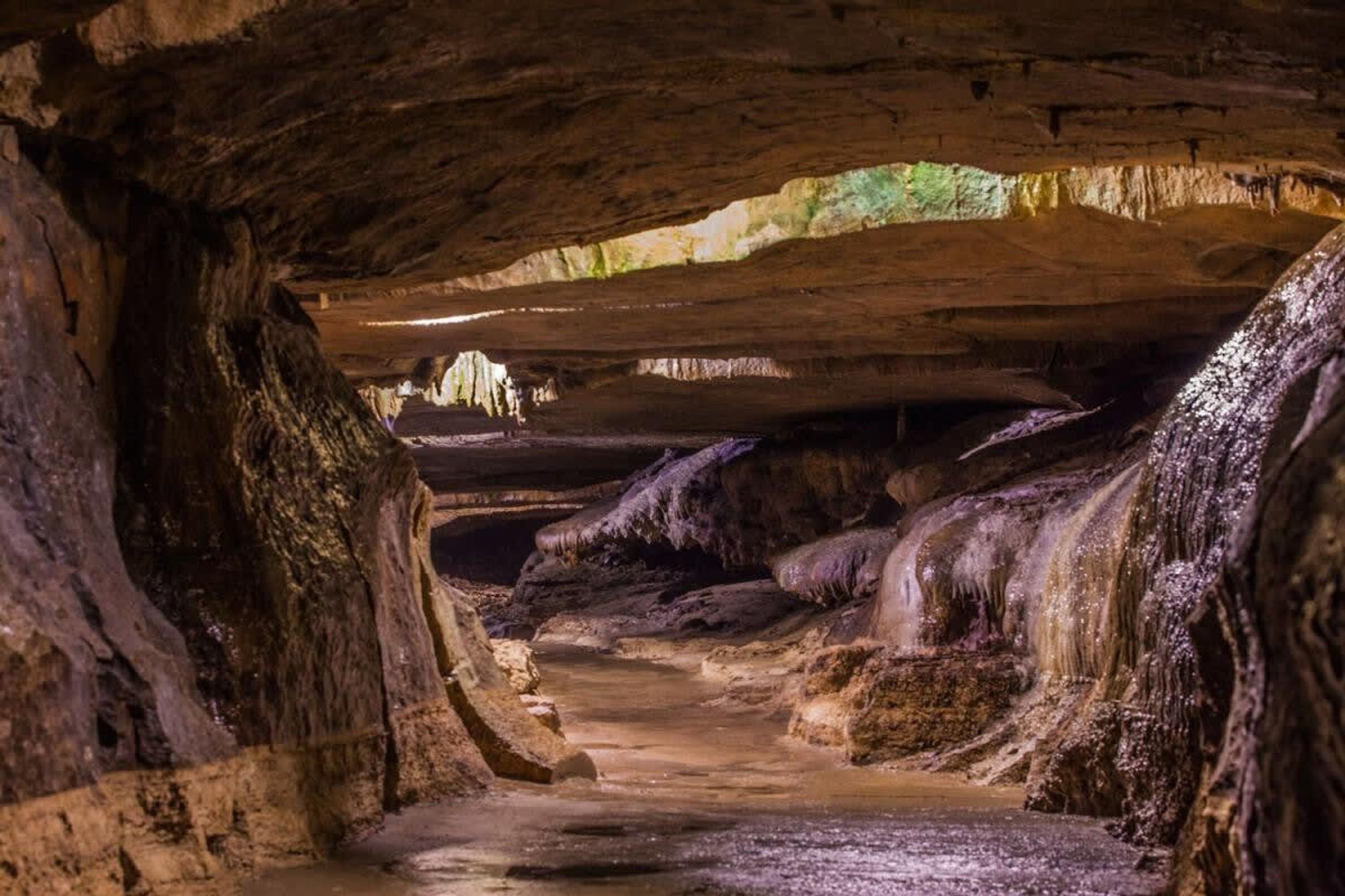 Una grotta con stalattiti e stalagmiti, un passaggio stretto e una cascata.