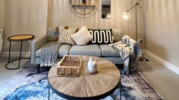 A cozy living room with a grey sofa, round coffee table, and a hanging light fixture.