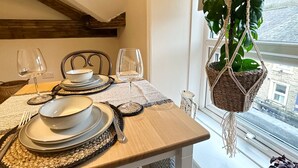 Una tavola apparecchiata con piatti, ciotole, posate e bicchieri da vino, con una pianta pensile e vista sulla città attraverso una finestra.