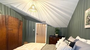 Una camera da letto con soffitto spiovente, un letto con molti cuscini, un armadio in legno e un comodino con una pianta.