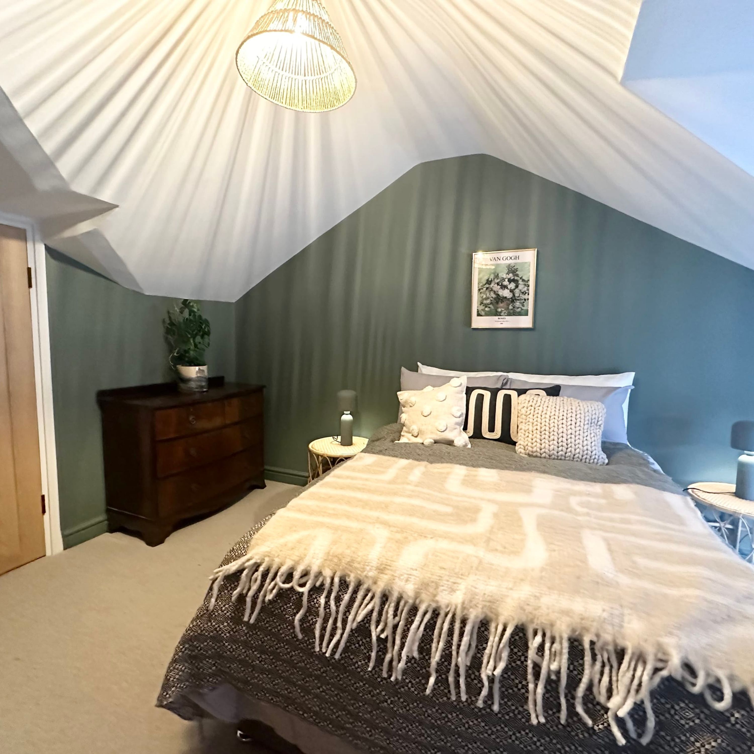 A bedroom with a sloped ceiling, a bed with patterned bedding, a nightstand, a dresser, and a framed picture on the wall.