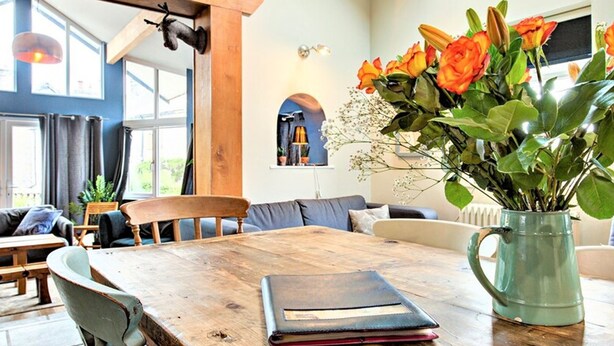 Un comedor con una mesa de madera, sillas y un florero con flores.