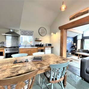 A modern kitchen with a wooden dining table, chairs, and a view into the living area.