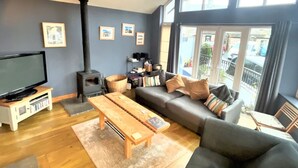 Una sala de estar moderna con un sofá, una mesa de centro de madera, un mueble para la televisión, una chimenea y ventanas grandes.