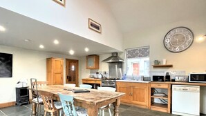 Una cocina amplia con armarios de madera, una mesa de comedor y sillas. Hay un reloj en la pared y un microondas en la encimera.
