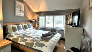Un dormitorio con cama, televisor, radiador y ventana.