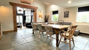 Un comedor amplio con una gran mesa de madera y seis sillas, piso de baldosas de piedra y vistas al exterior a través de una ventana.