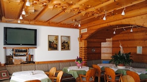 Un restaurant au décor intérieur en bois, avec des tables recouvertes de nappes vertes et un téléviseur accroché au mur.