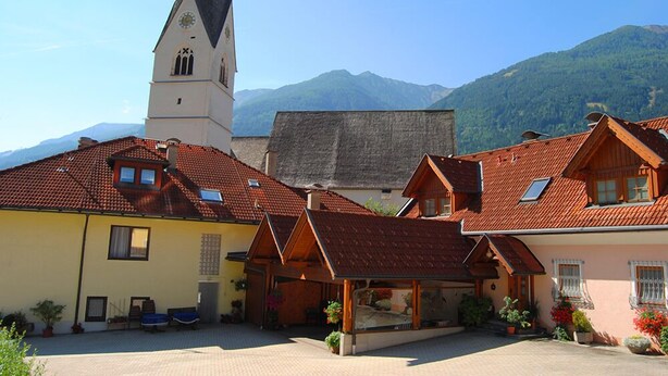 Un village européen traditionnel, avec un clocher d’église, des maisons en bois et une cour pavée.