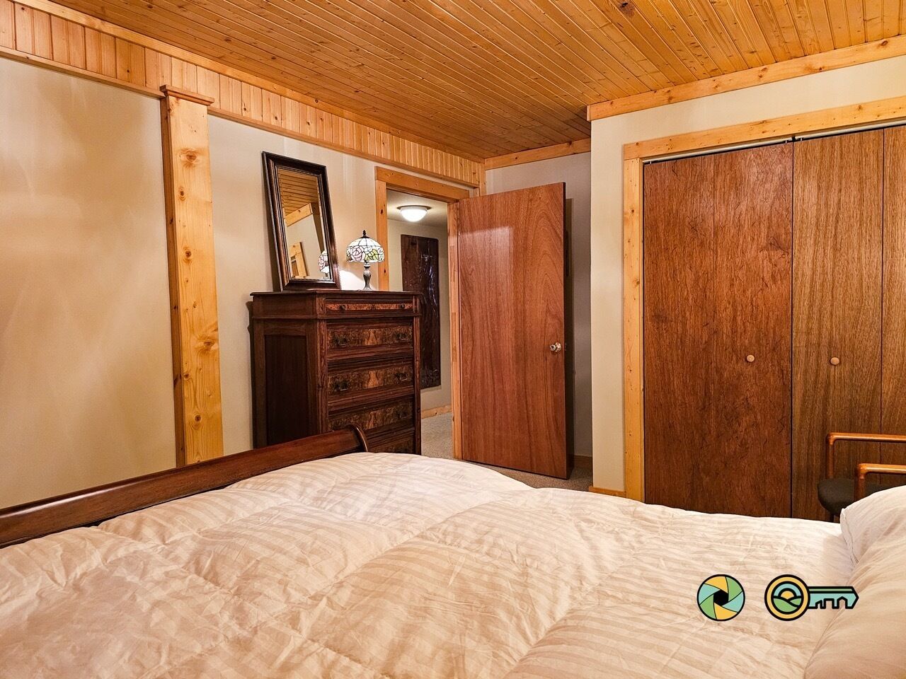 Un dormitorio con techo de madera, una cama con edredón blanco, un aparador de madera y un armario.