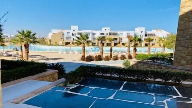 A resort with a pool, palm trees, and modern buildings. - Ground Spacious 1-BR Apt @ SwanLake - El Gouna (Red Sea Governorate)