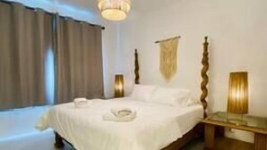 A bedroom with a wooden bed, white linens, a bedside table with a lamp, and a hanging light fixture. - Ground Spacious 1-BR Apt @ SwanLake - El Gouna (Red Sea Governorate)