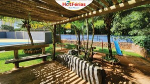 Un espacio al aire libre cubierto con piscina, bancos de madera y un parque infantil.