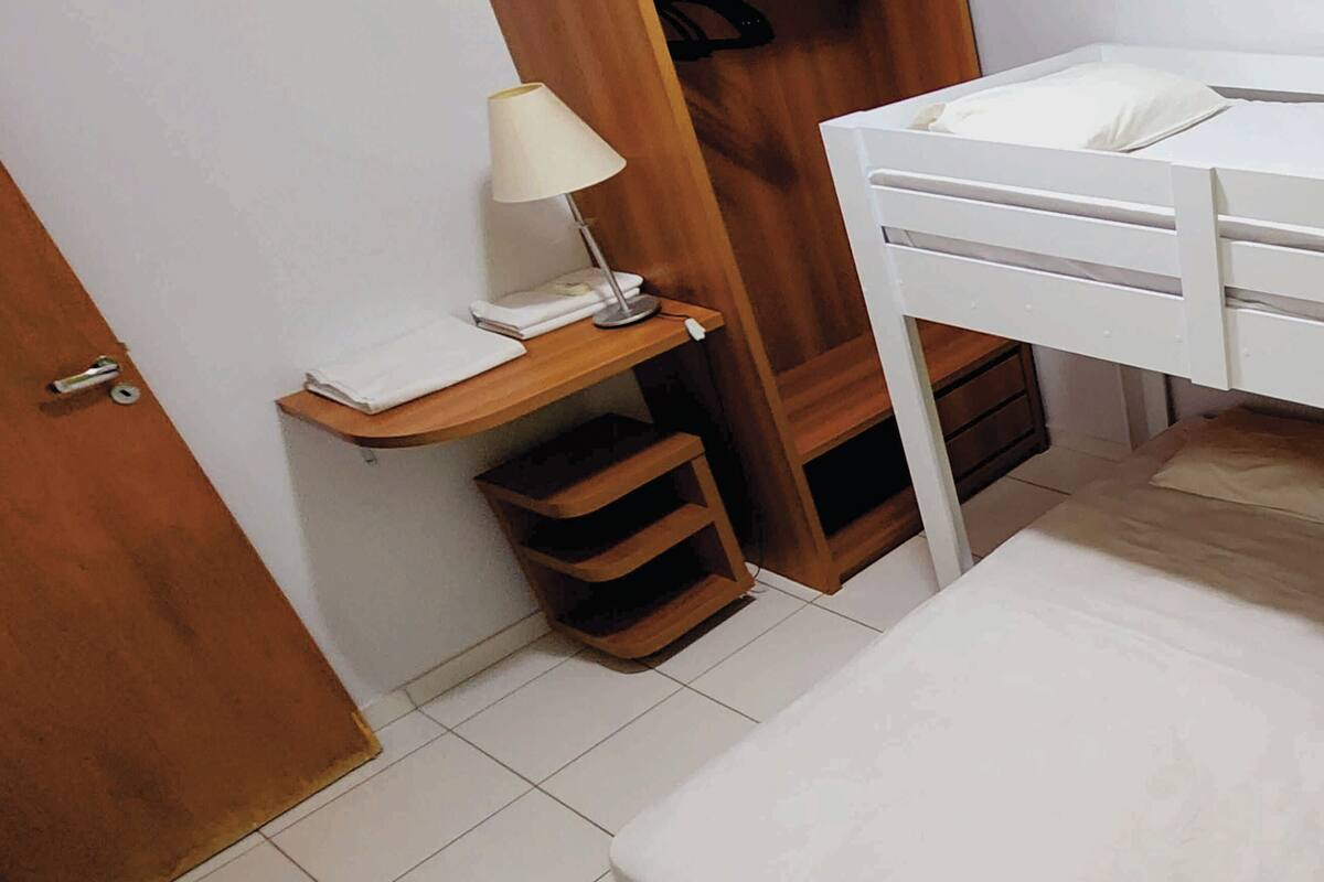 Une petite pièce, bien rangée, avec un lit superposé, une table de chevet avec une lampe et une étagère en bois.