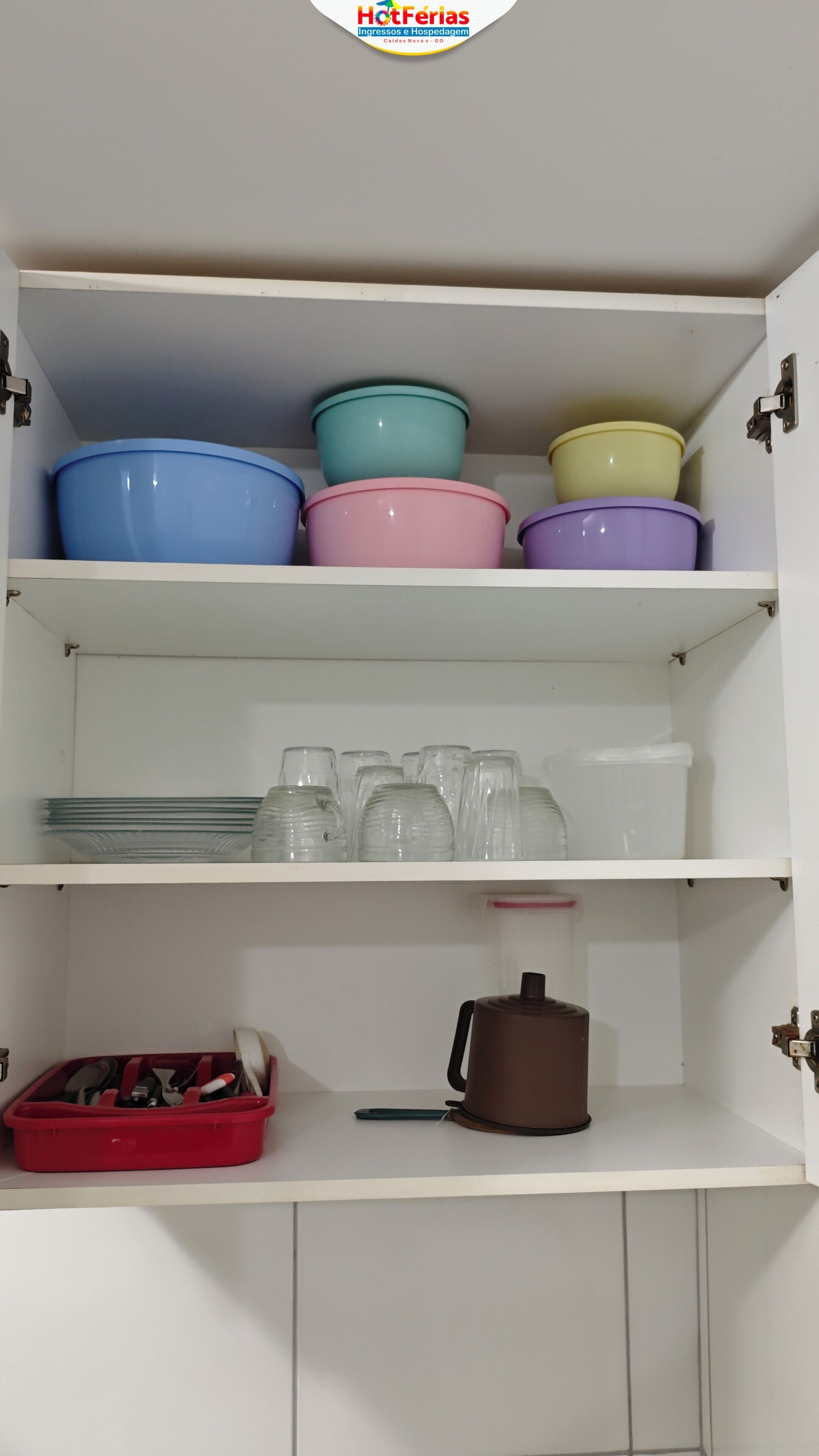 A kitchen cabinet with storage shelves containing bowls, plates, and a coffee pot.
