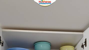 A kitchen cabinet with storage shelves containing bowls, plates, and a coffee pot.