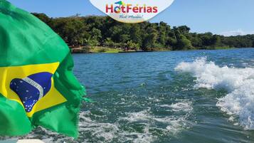 A flag waving in the wind, a body of water, and a forested shoreline.
